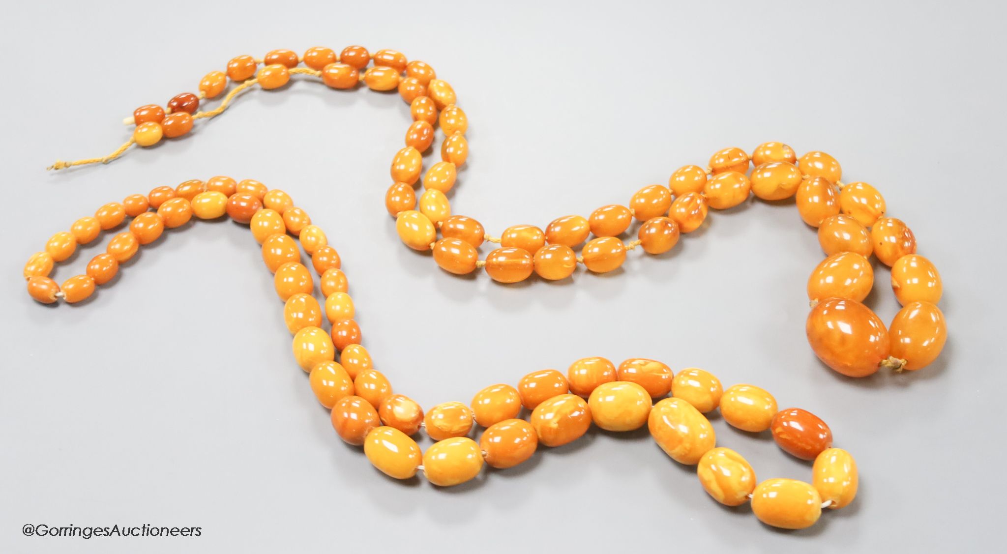 Two single strand graduated oval amber bead necklaces, 71cm, 61 grams & 89cm, 68 grams (beads missing from larger necklace)